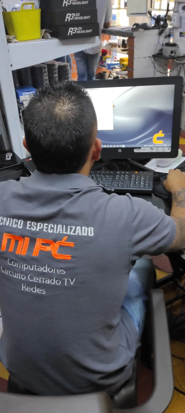 Técnico de MiPC Tecnología, de espaldas y con uniforme de la empresa, revisa un computador de escritorio en el taller